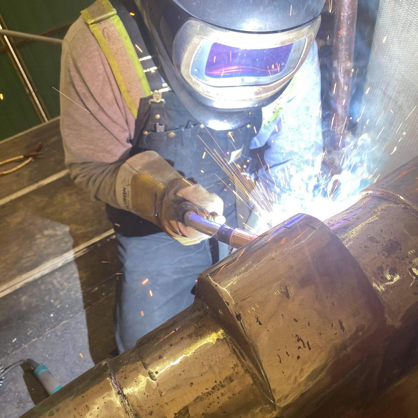 A man wearing a welding helmet is welding a pipe