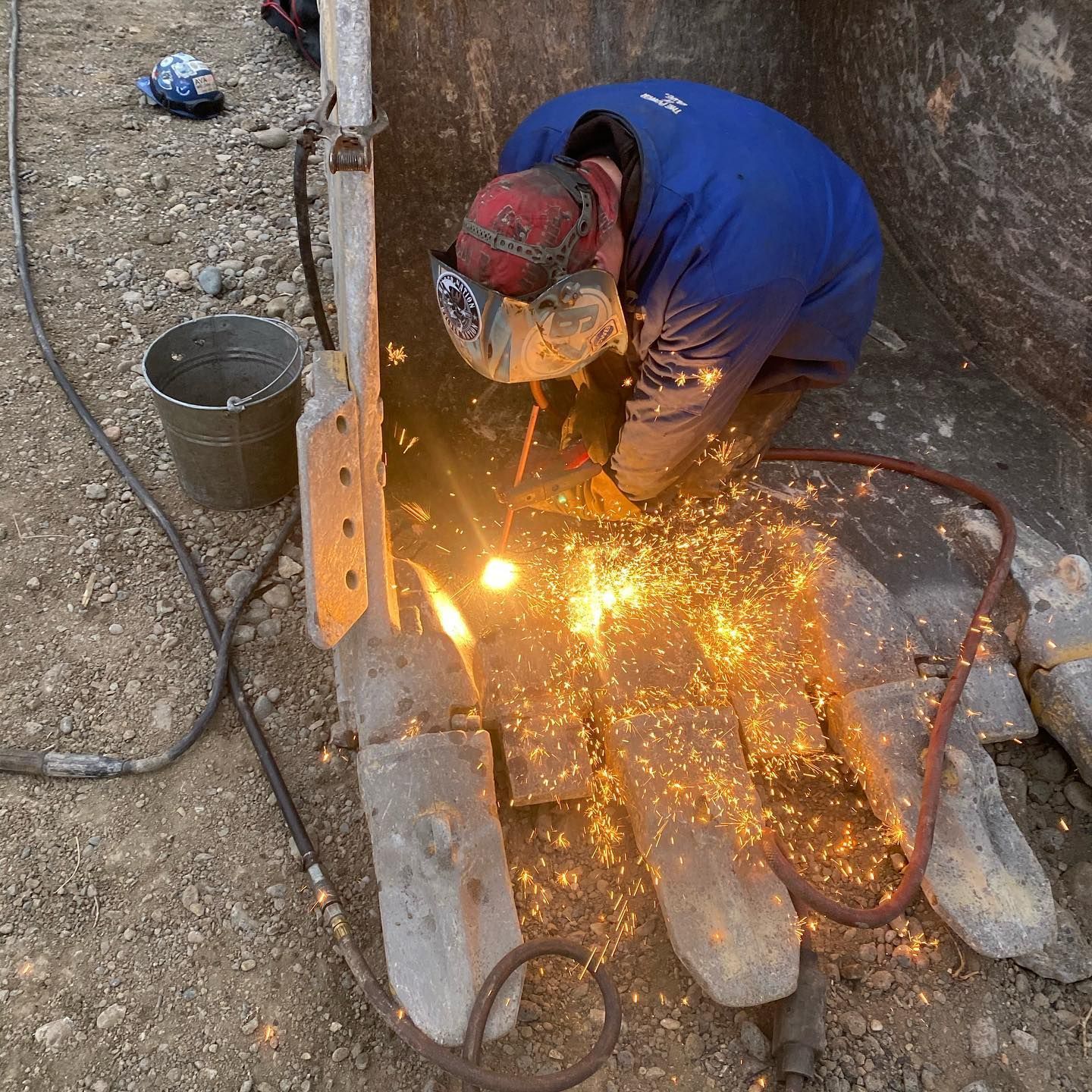 A man in a blue jacket is welding a piece of metal