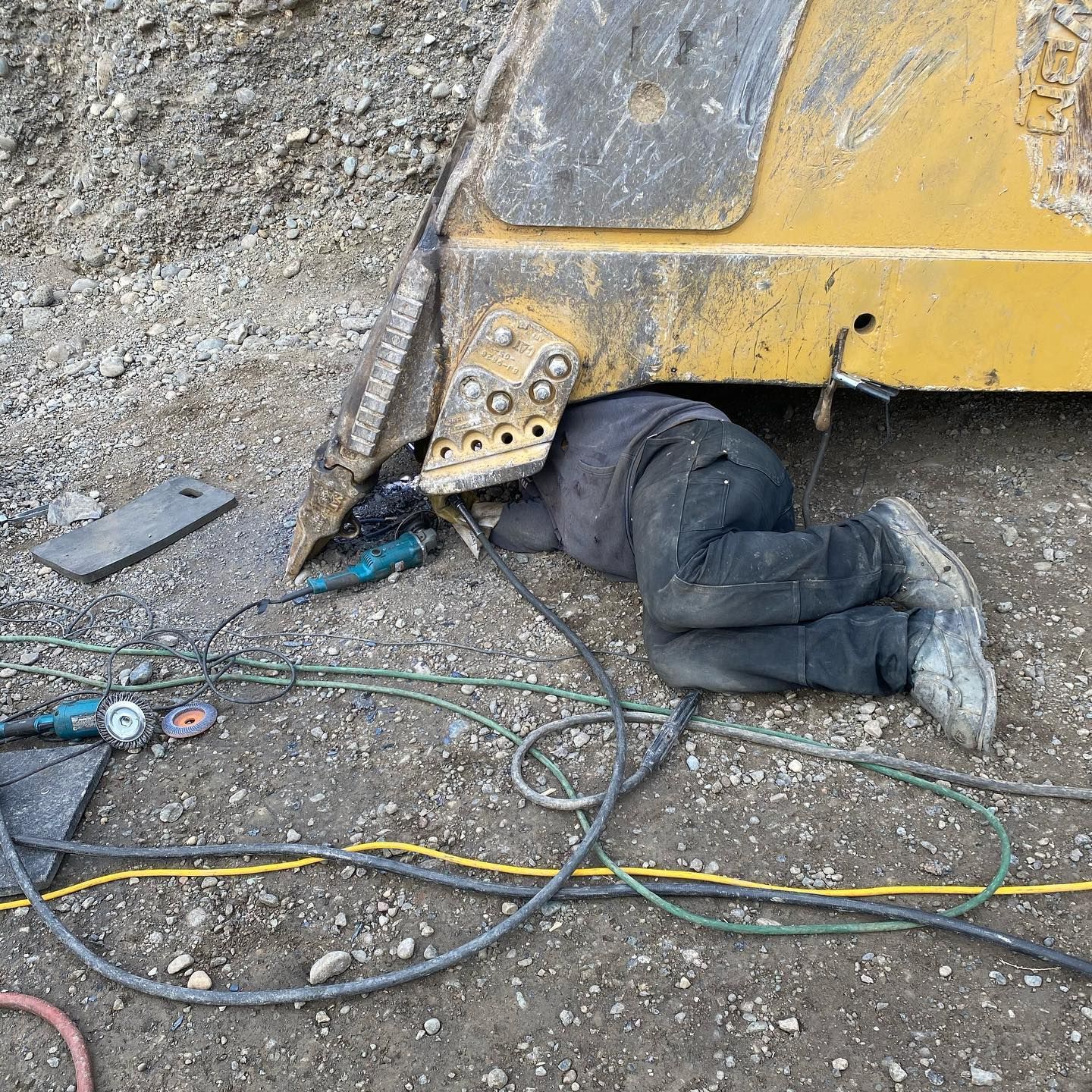 A man is laying on the ground under a bulldozer.