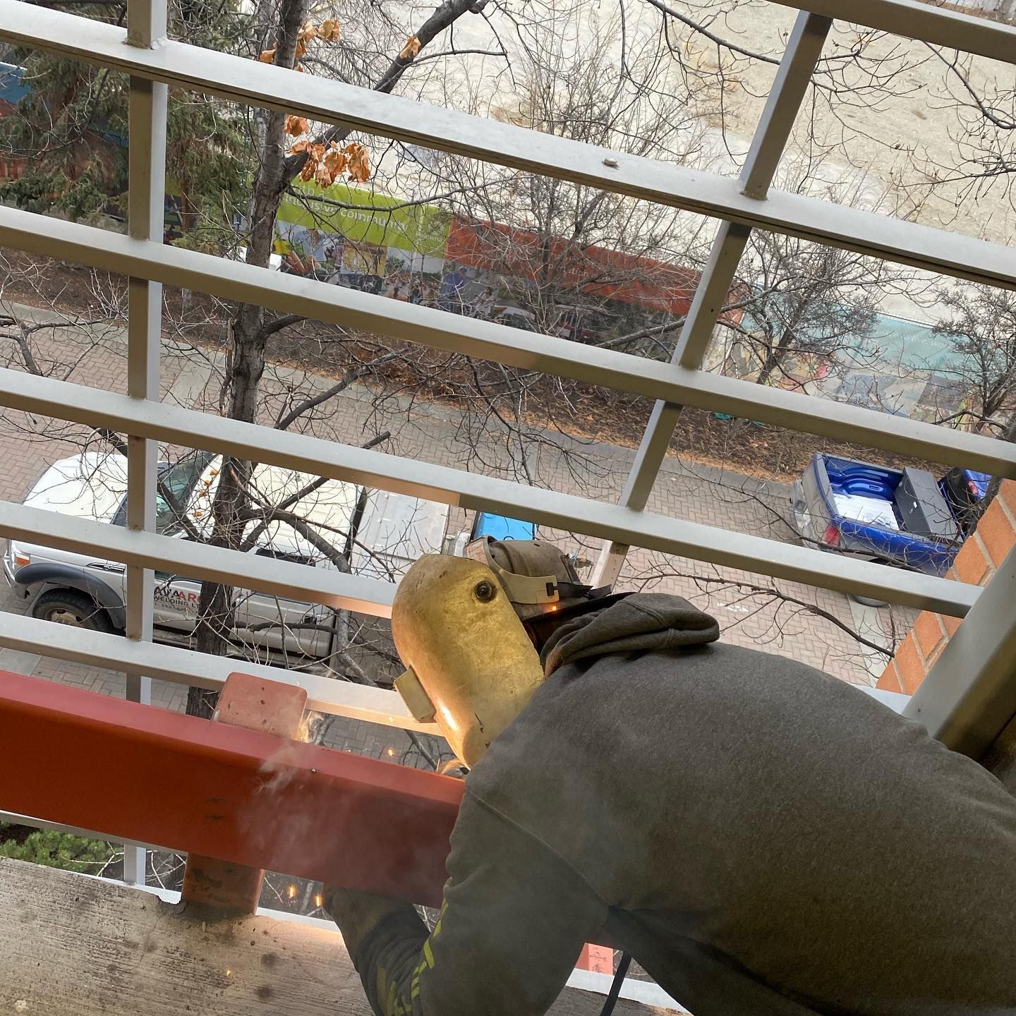 A man wearing a welding mask is working on a railing