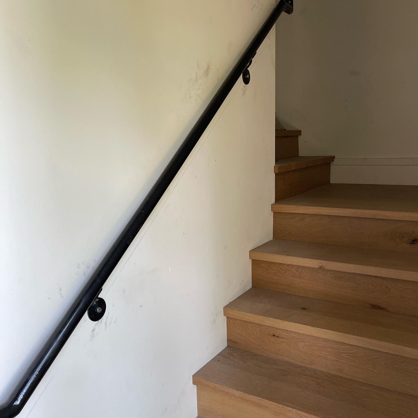 A wooden staircase with a black railing against a white wall