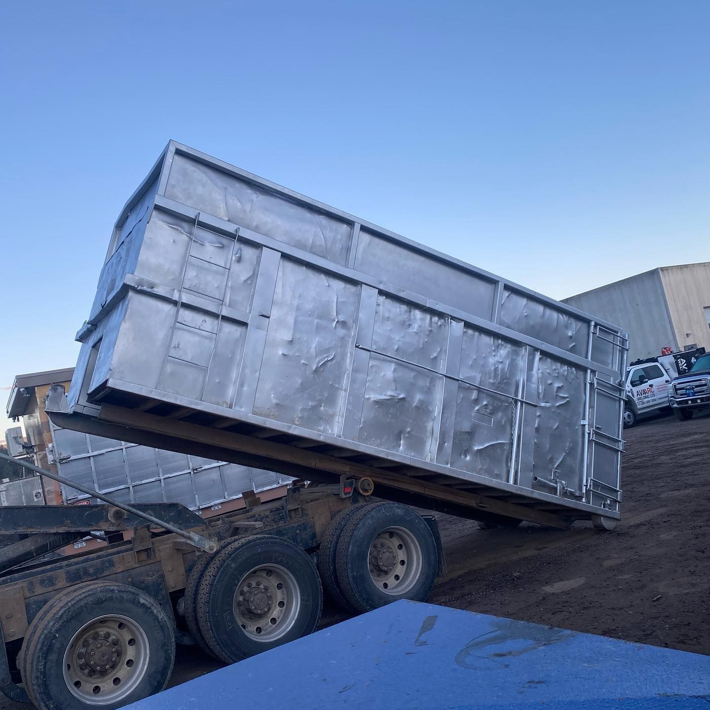A dump truck is being loaded with a large metal container.