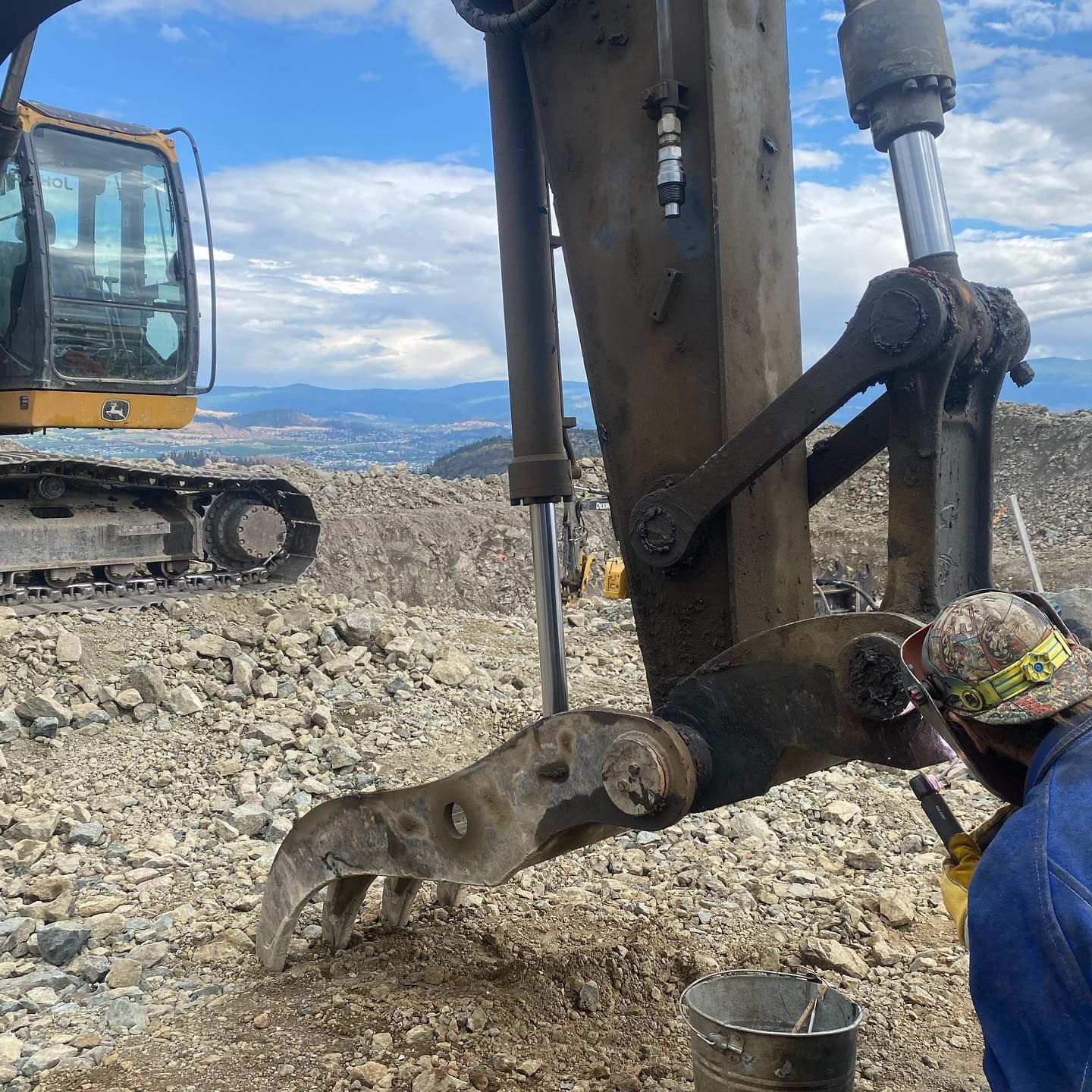 A man is working on a large excavator on a rocky hillside.