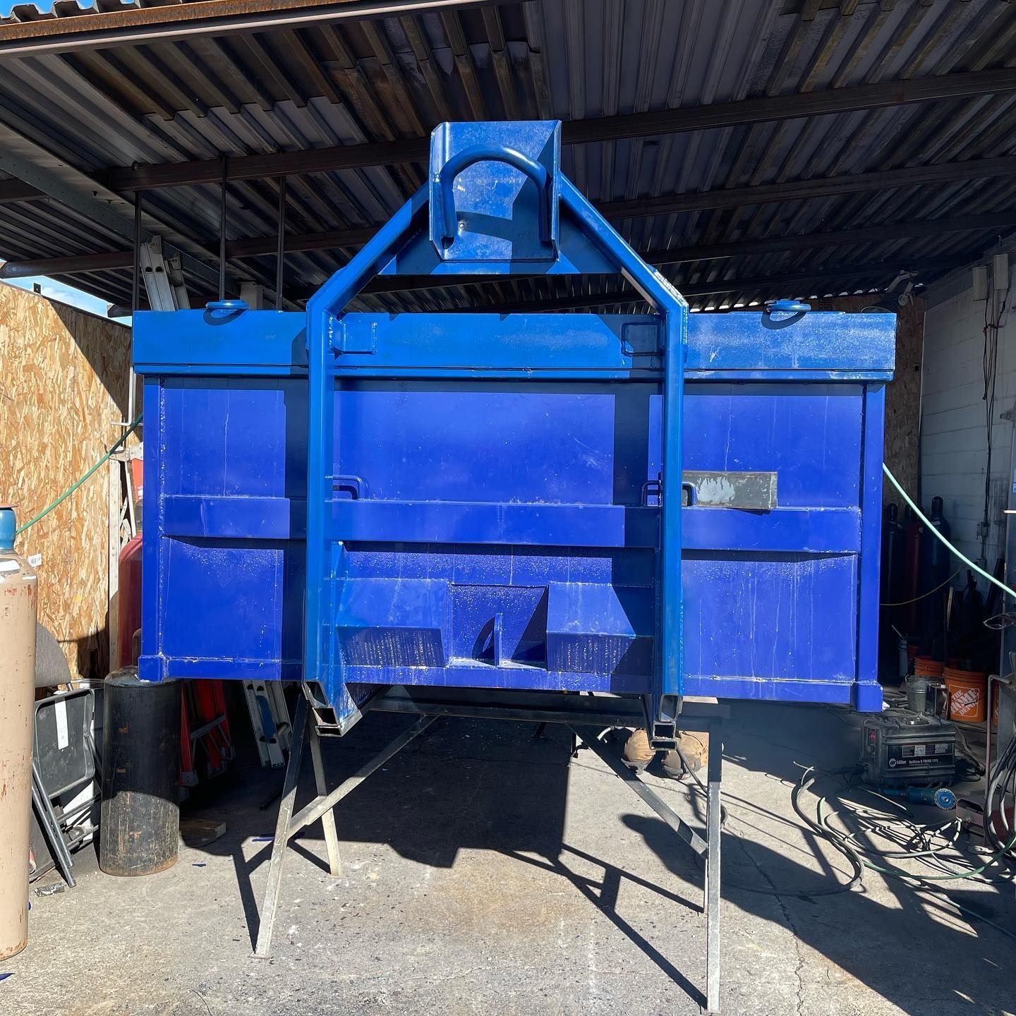 A blue dumpster is sitting under a roof in a garage