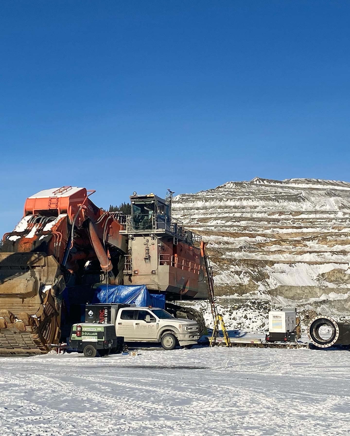 A large bulldozer is parked in the snow in front of a mountain.