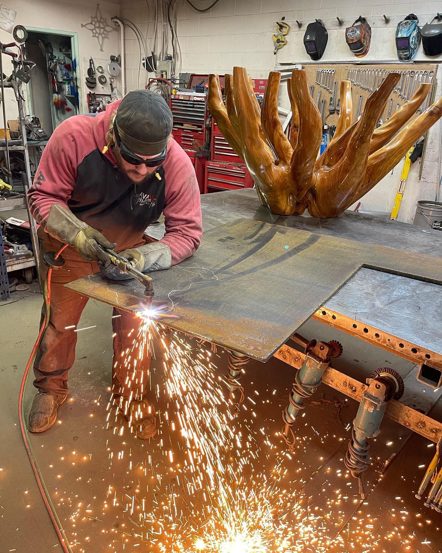 A man is cutting a piece of metal with a torch in a workshop.