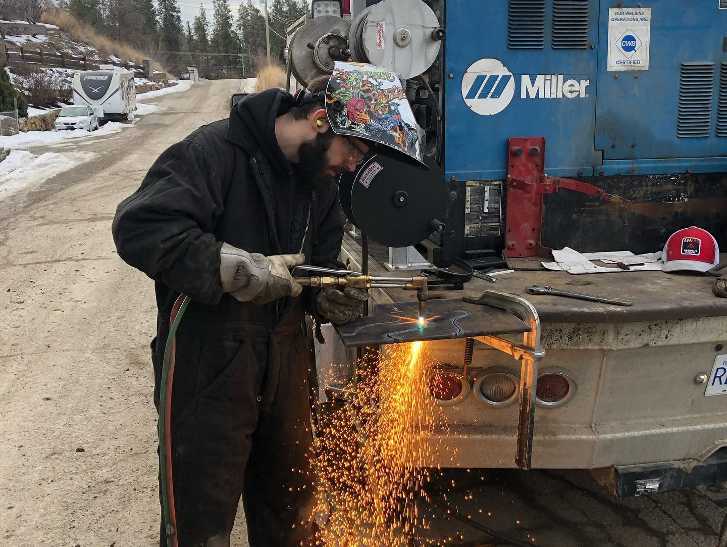 A man is cutting a piece of metal in front of a miller truck