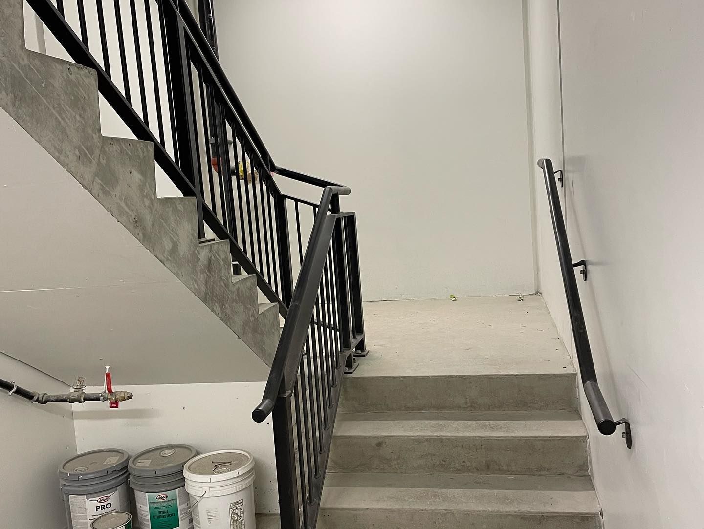 A staircase with a metal railing and buckets of paint on the floor.