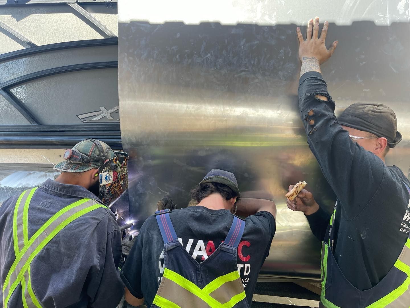 A group of men are working on a stainless steel tank.
