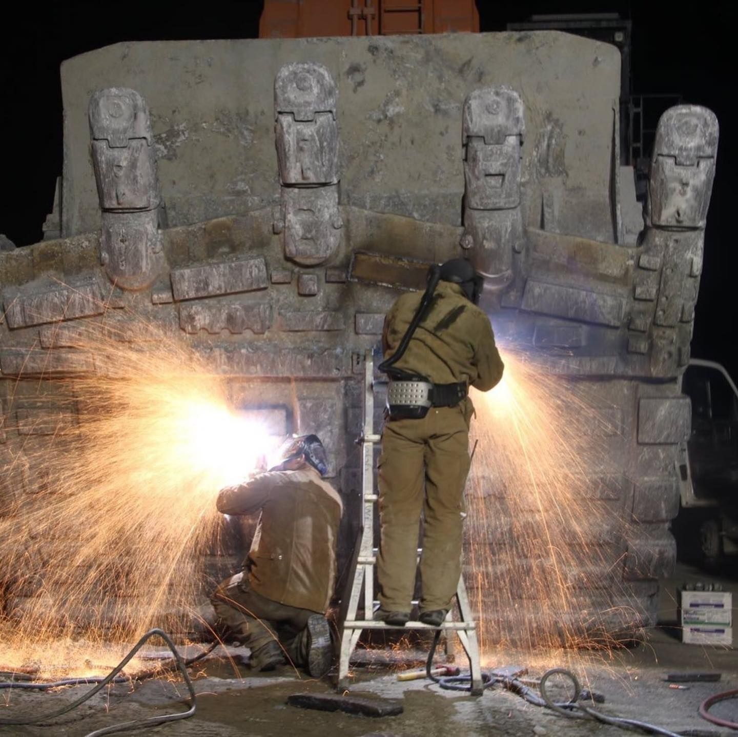 Two men are welding a large piece of metal with sparks coming out of it