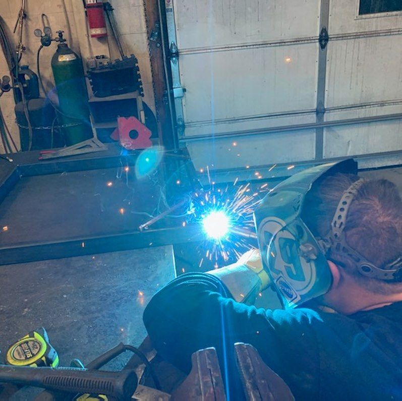 A man wearing a welding mask is welding a piece of metal.