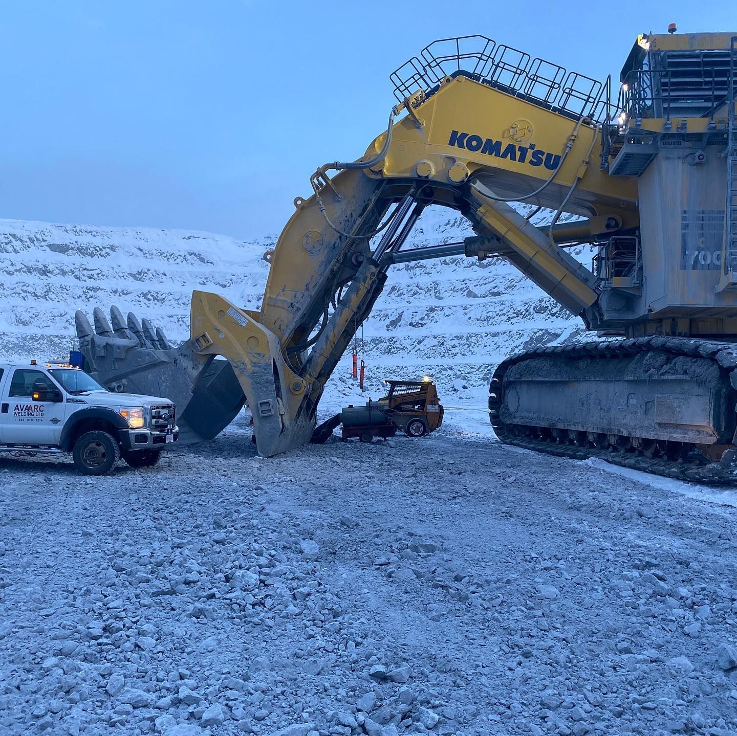 A komatsu excavator is sitting in the snow next to a truck