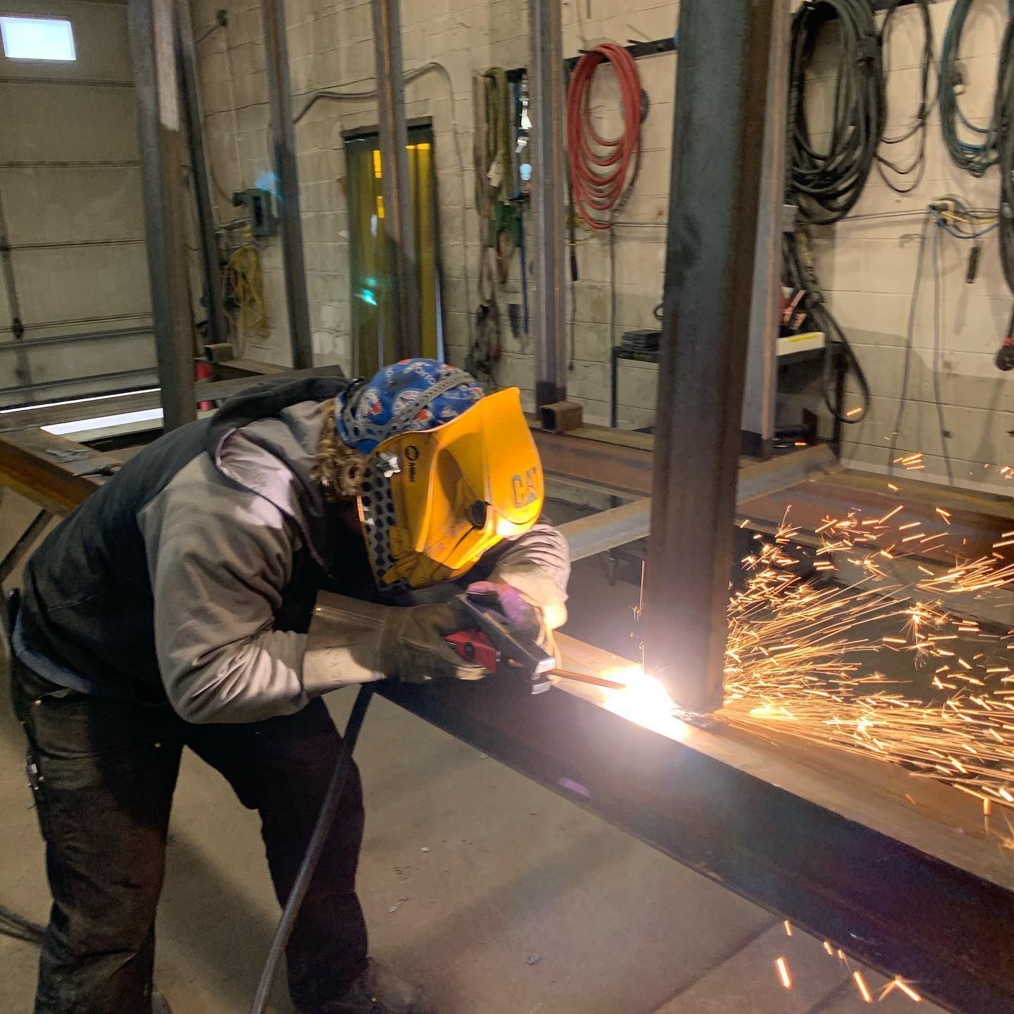 A man wearing a welding helmet is welding a piece of metal