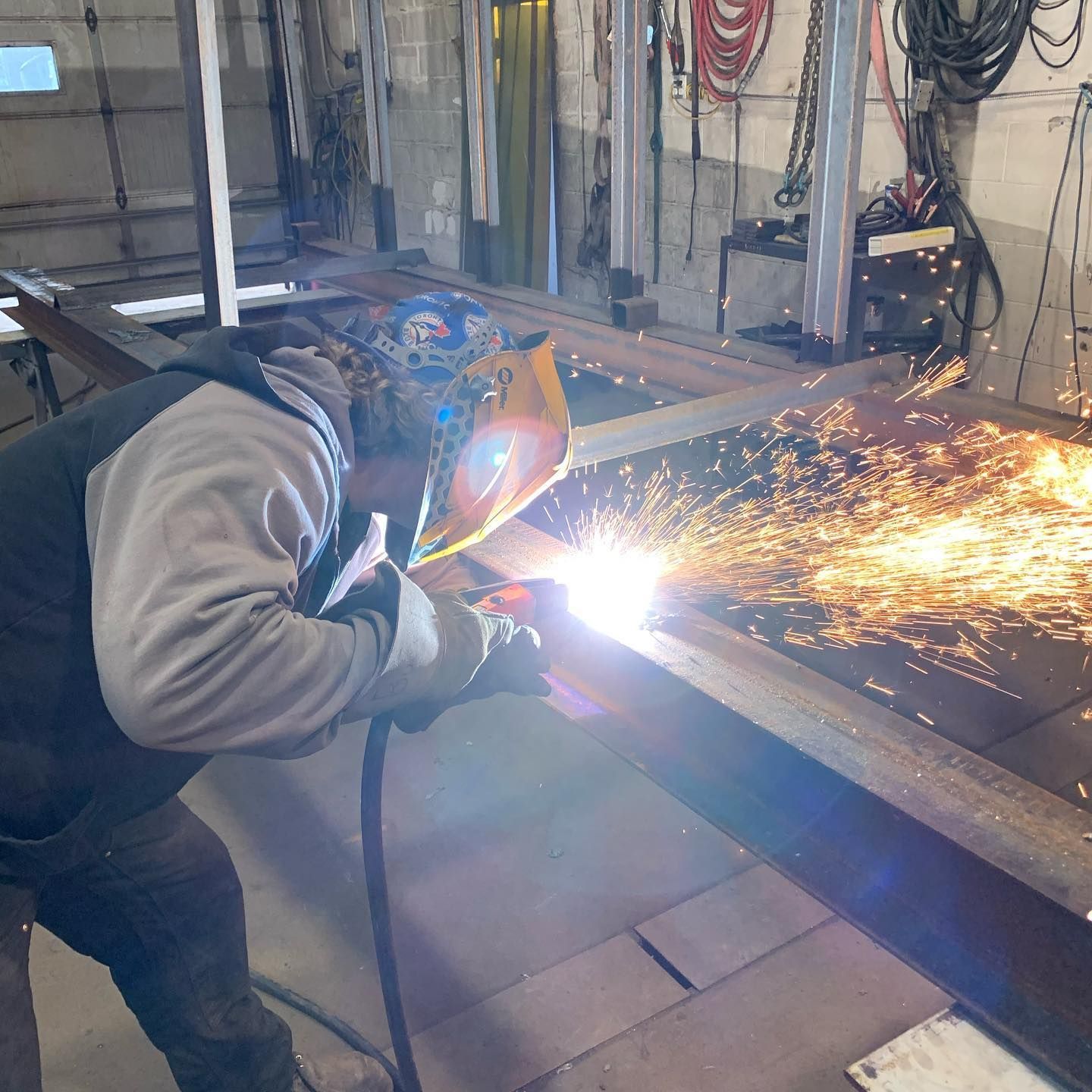 A man wearing a welding helmet is welding a piece of metal