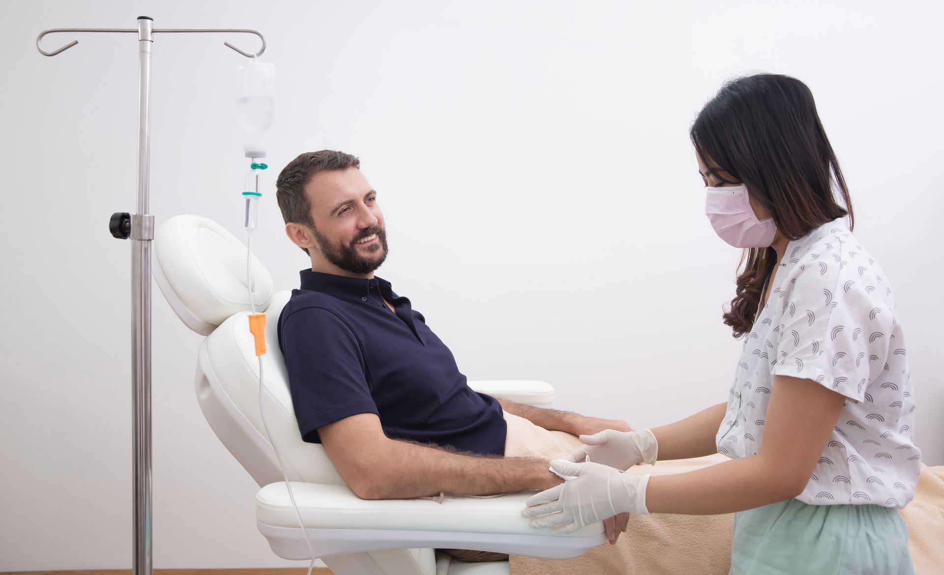 Patient and nurse in a clinic, with the nurse holding the patient’s hand near an IV stand