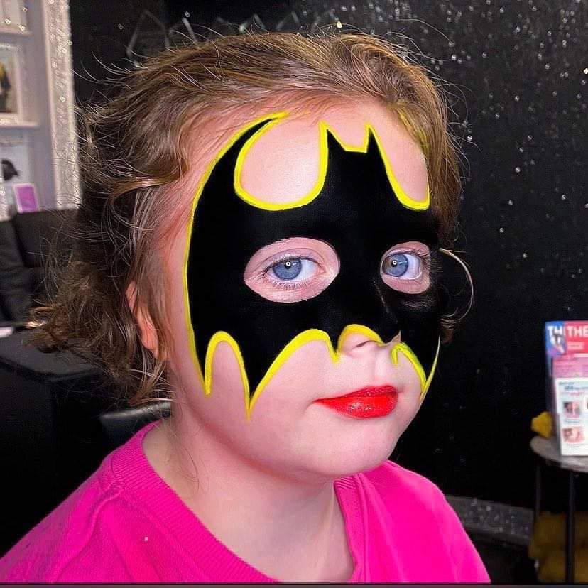 a little girl with a batman mask painted on her face