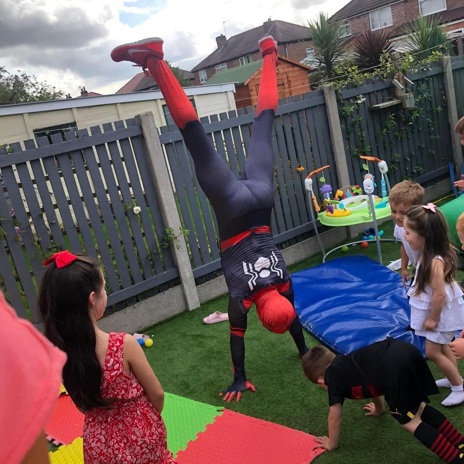 a man in a spiderman costume is doing a handstand in front of a group of children .