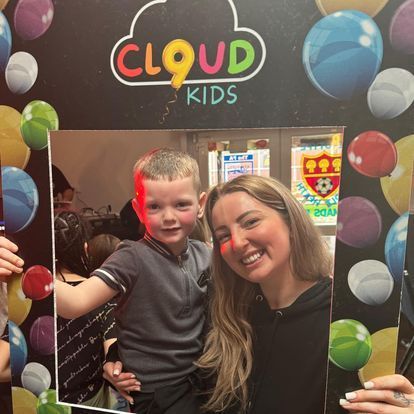 a woman holding a picture frame with a child in front of a cloud kids sign