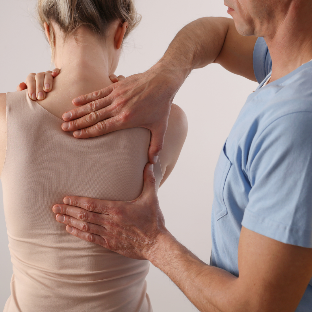 A healthcare professional examines a patient's back. Hands palpate the shoulder and spine areas.