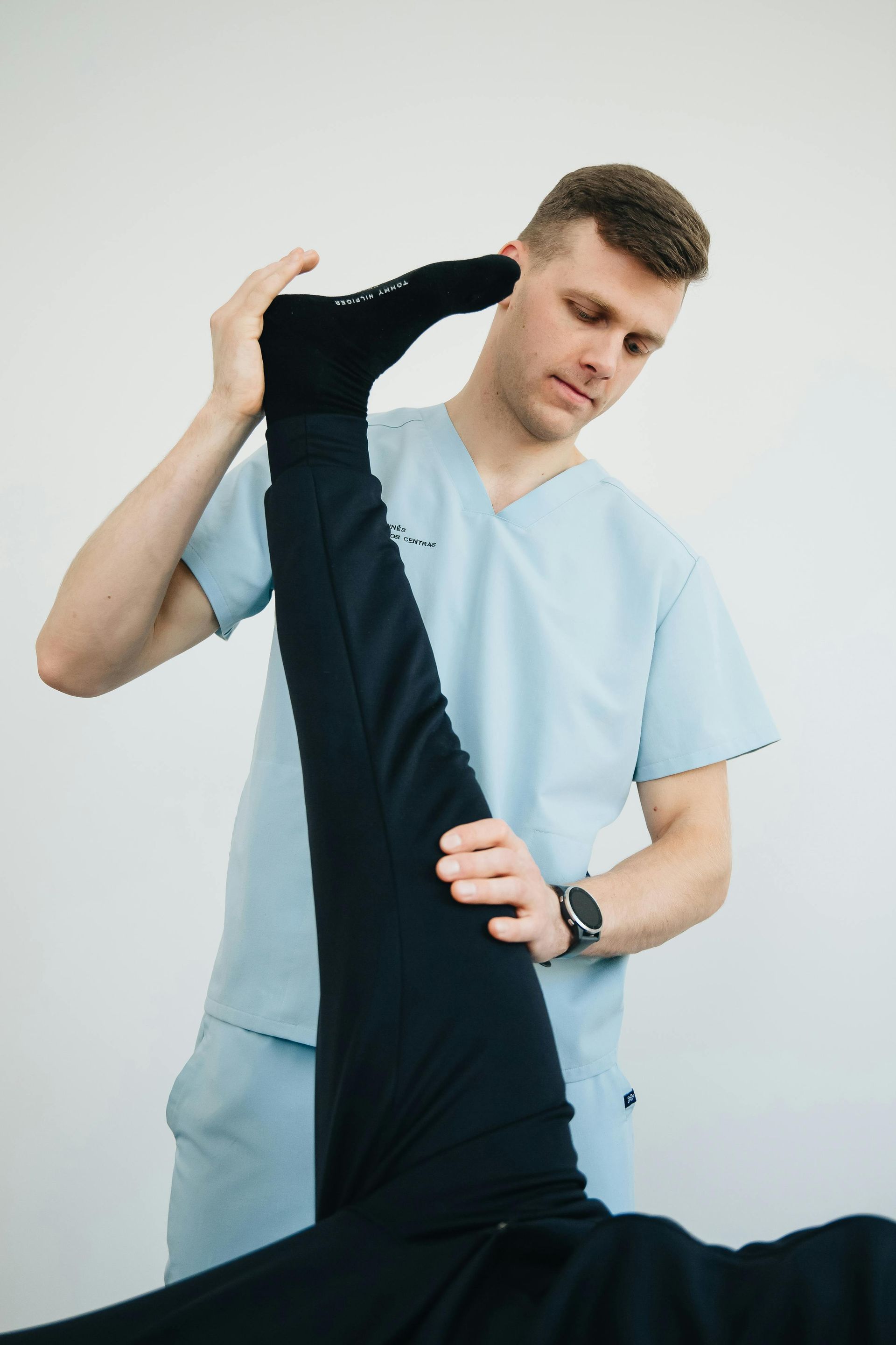Physiotherapist stretching a patient's leg. In a white room, man in scrubs holding a leg upright.