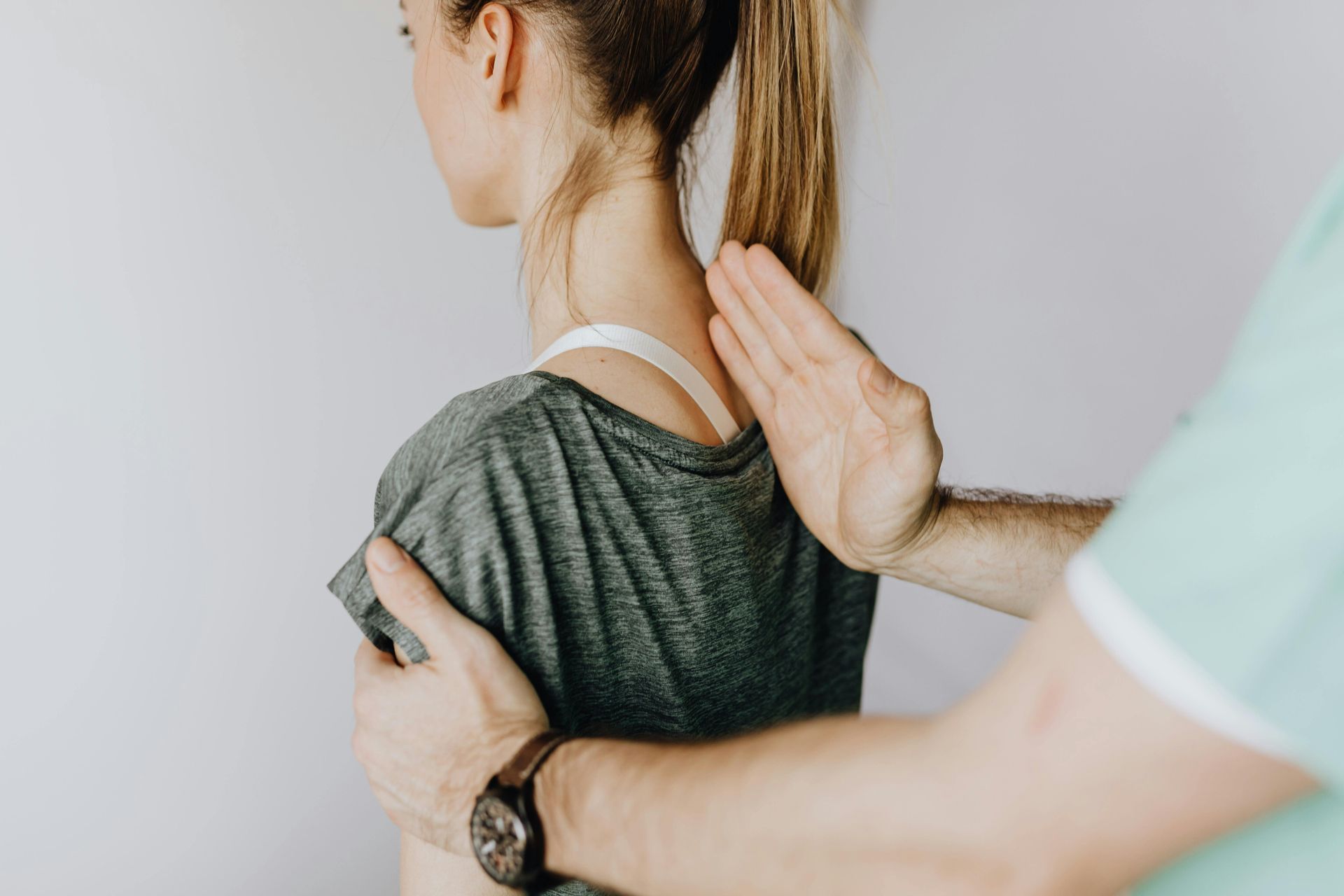 A person's back being examined by someone's hands. They are in a room with a light wall.