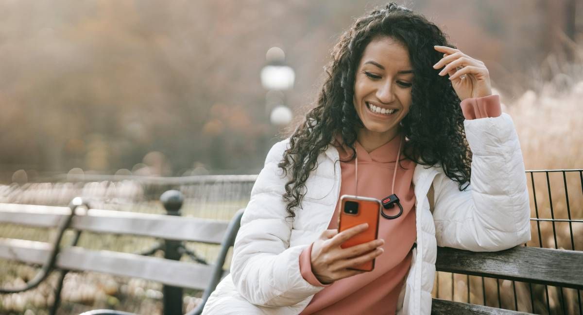 Lady smiling on a park bench while reading a text message 
