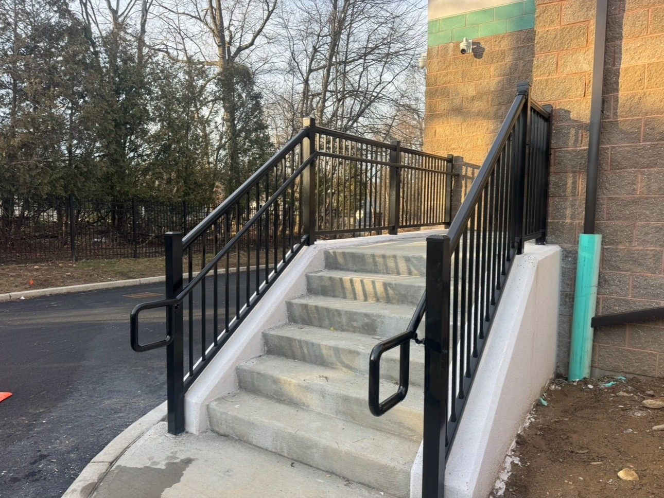 Concrete outdoor steps with black metal railings leading up to a building entrance.