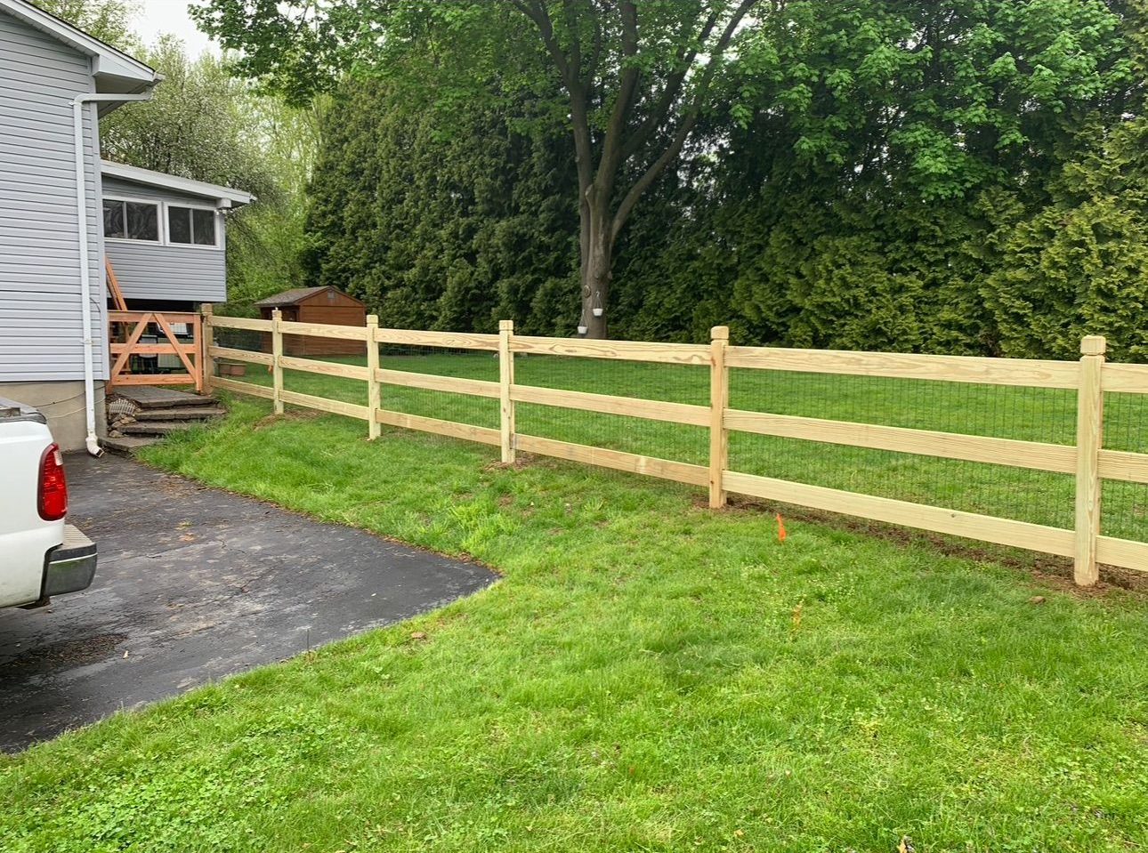 A horizontal wooden slat privacy fence stands in a grassy backyard with trees in the background.