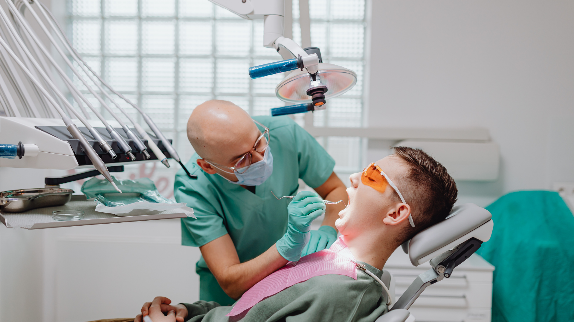 Dentist examining patient's teeth with tools in a dental office. The patient wears safety glasses.