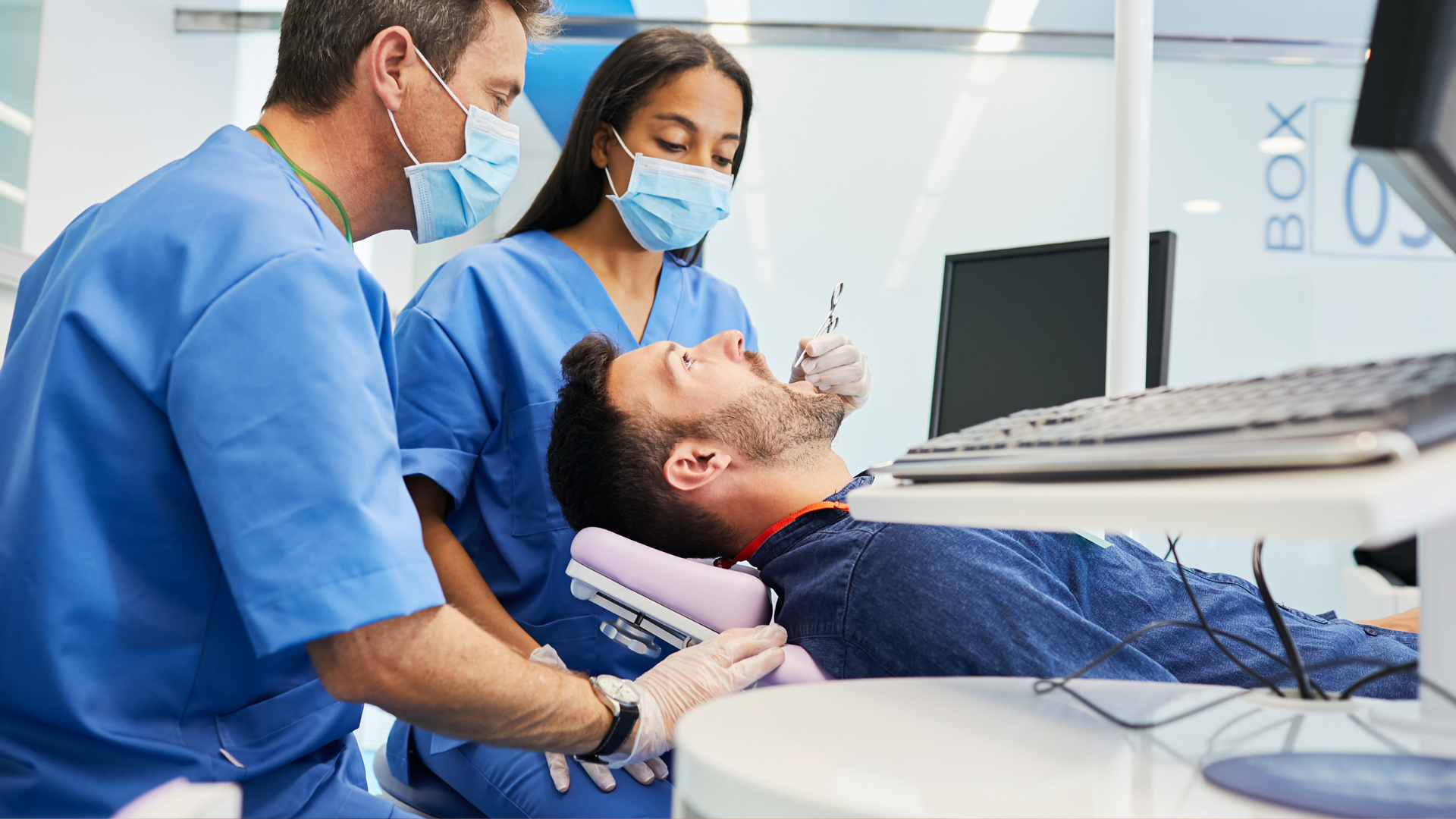 Dentist and assistant examining a patient in a dental chair with equipment nearby