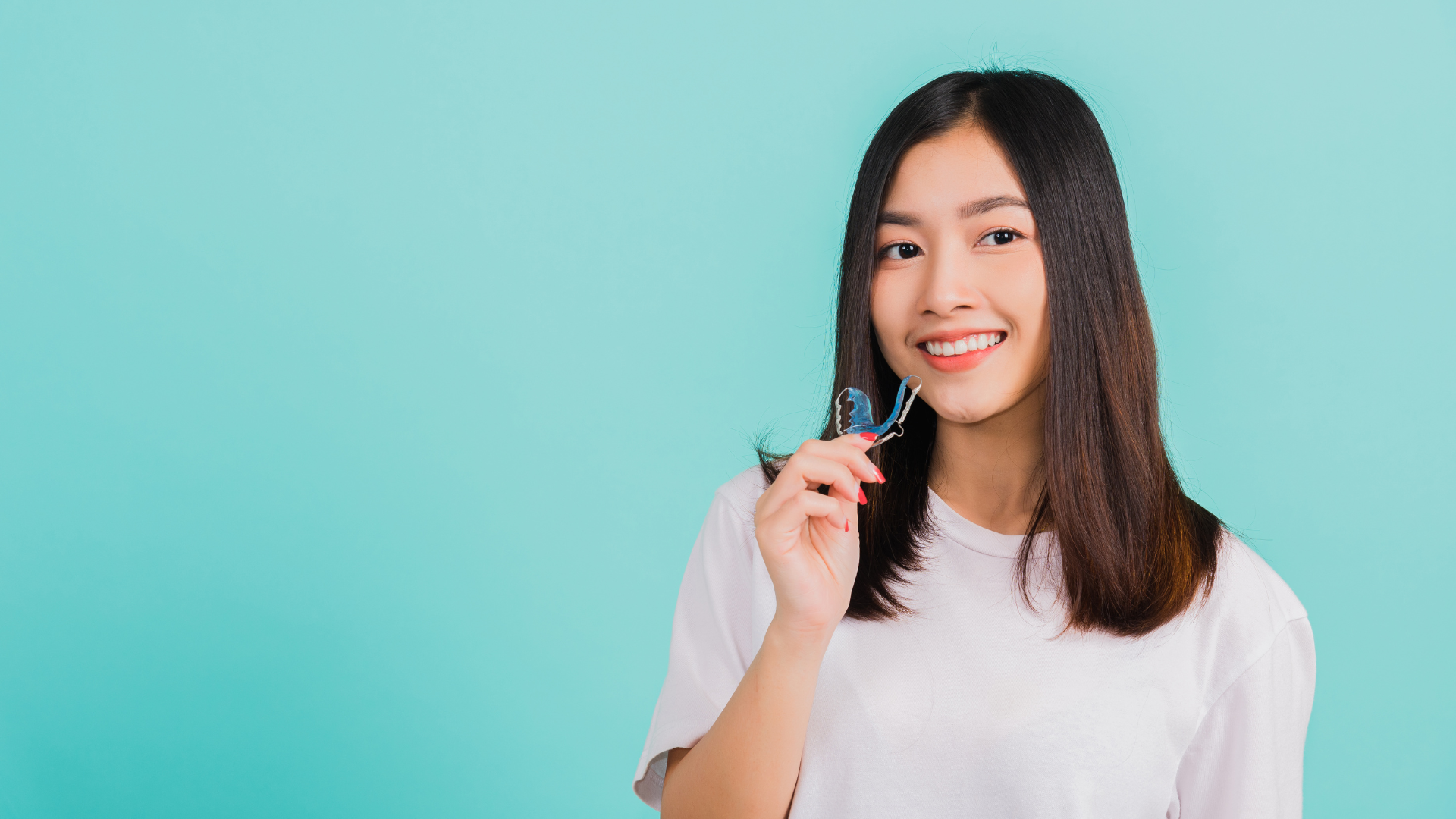 A young woman is holding a clear brace on her teeth.