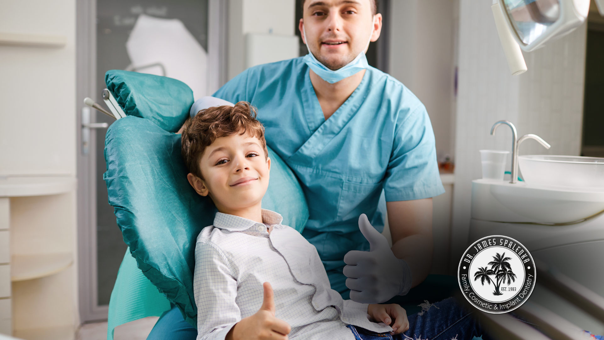 A young boy is sitting in a dental chair giving a thumbs up.