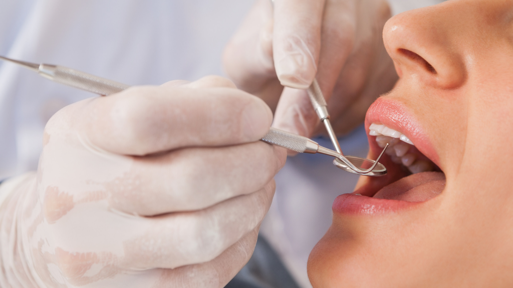 Dentist's gloved hands examining patient's teeth with dental tools, mouth open.