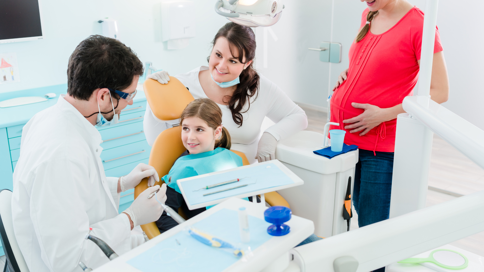 Dentist examining a child's teeth in a dental office; a pregnant woman and another woman watch.