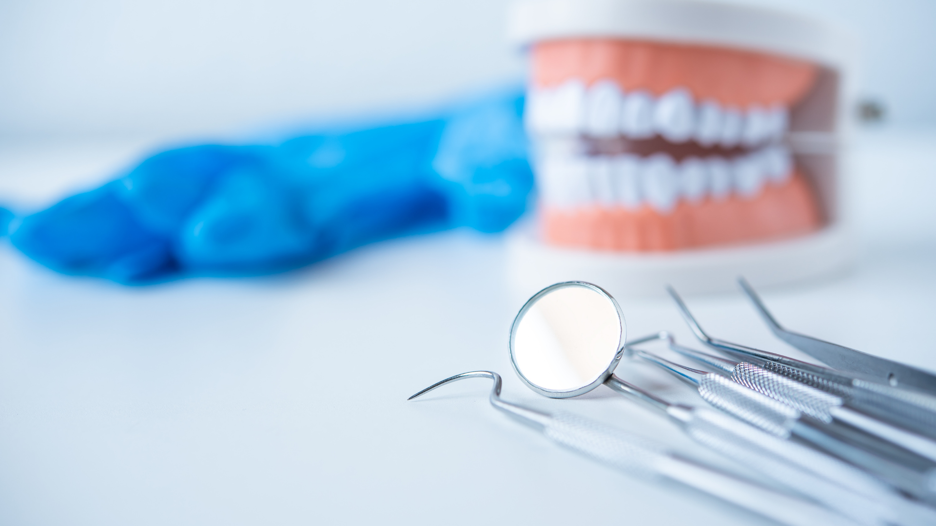 Dental mirror and tools beside a model of teeth on a blue surface