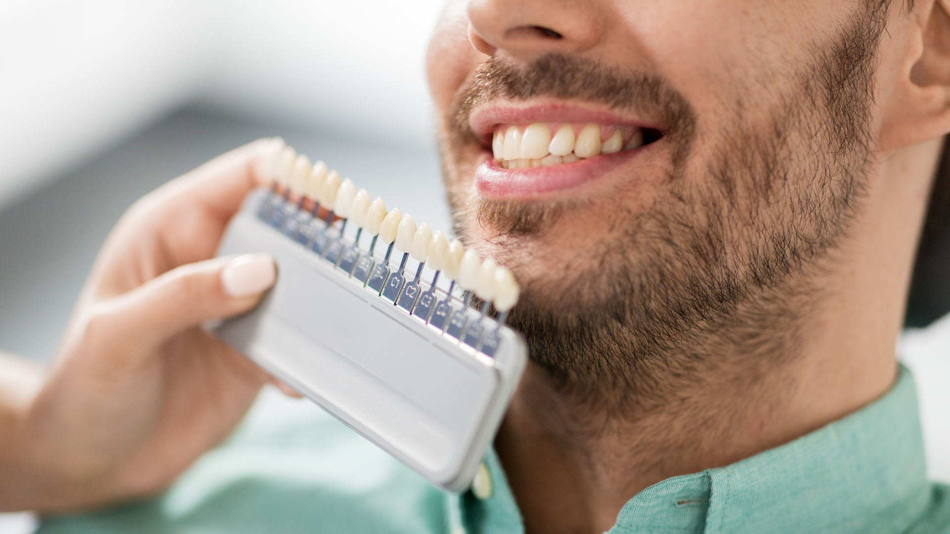 A man is holding a tooth color chart in front of his mouth.