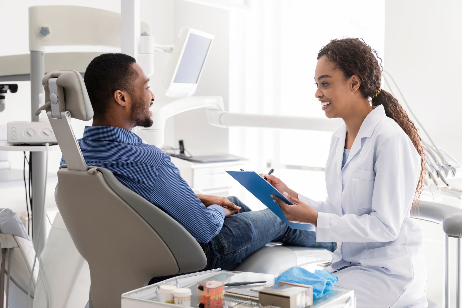 A man is sitting in a dental chair talking to a female dentist.