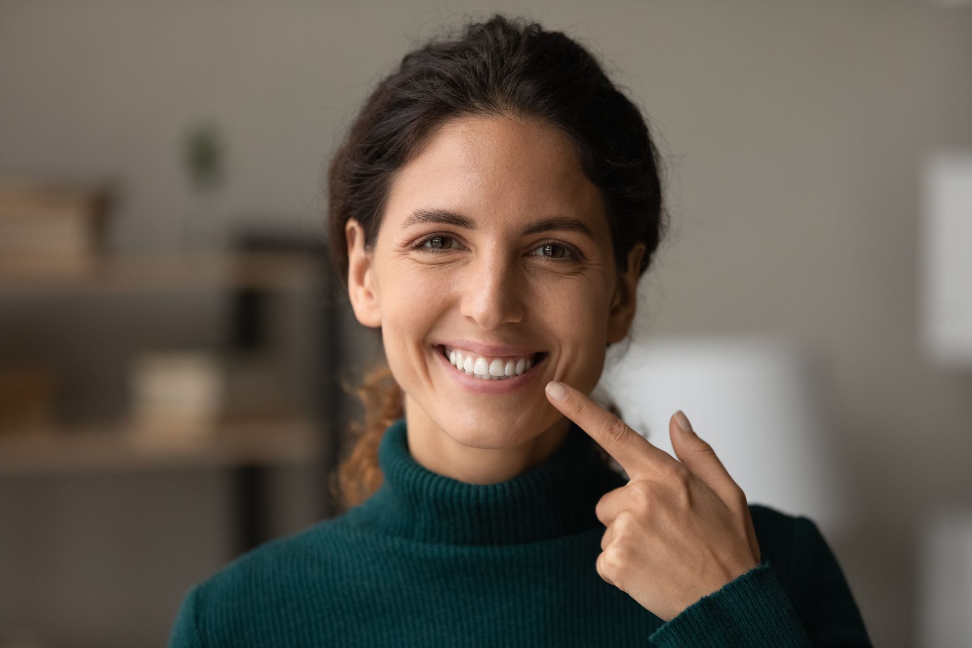 A woman is smiling and pointing at her teeth.