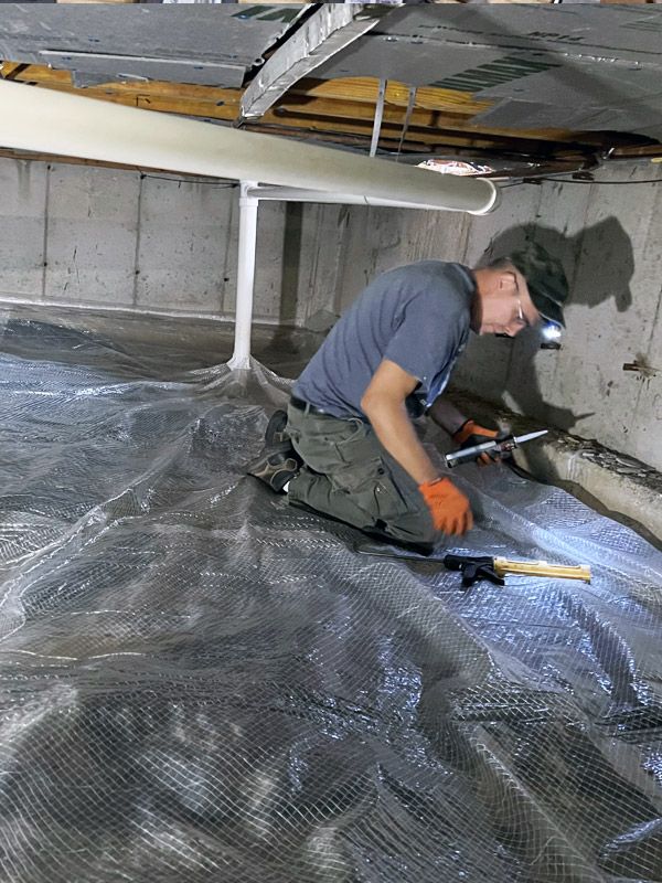 A man is kneeling down in a basement with a flashlight.