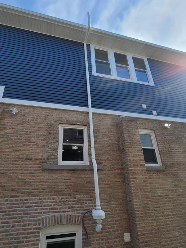 A brick building with a blue siding and a white pipe on the side of it.