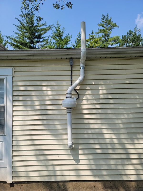 A white pipe is attached to the side of a house