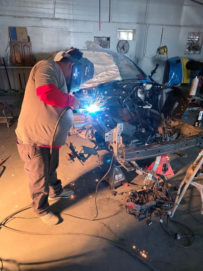 Person in green gloves spray painting a car white in a workshop.