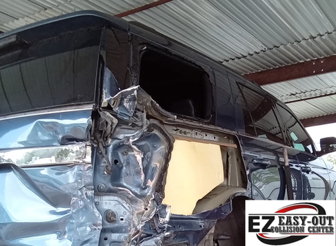 Damaged blue van's side with crushed frame; window broken. Collision damage, auto body shop setting.