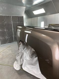 Truck bed being painted in a paint booth; brown paint, bright lighting, gray walls.