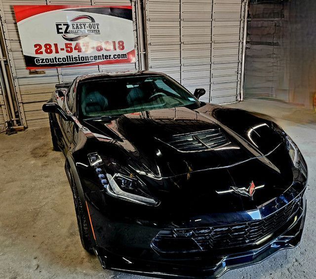 Black Corvette sports car in a garage with EZ Collision Center sign.