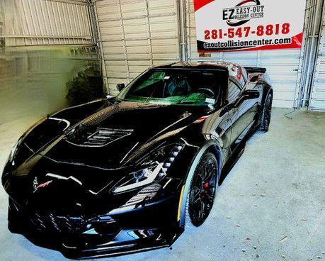 Black Corvette sports car in a garage, next to a sign for EZ Cut Collision Center.