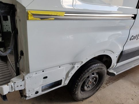 White van with dented rear quarter panel being repaired at a shop, showing new paint.