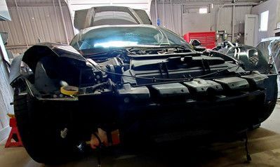 Black sports car in a repair shop with its hood and front panels removed.