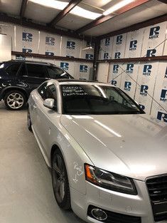 Silver Audi coupe and black SUV parked inside a garage with white and blue insulated walls.