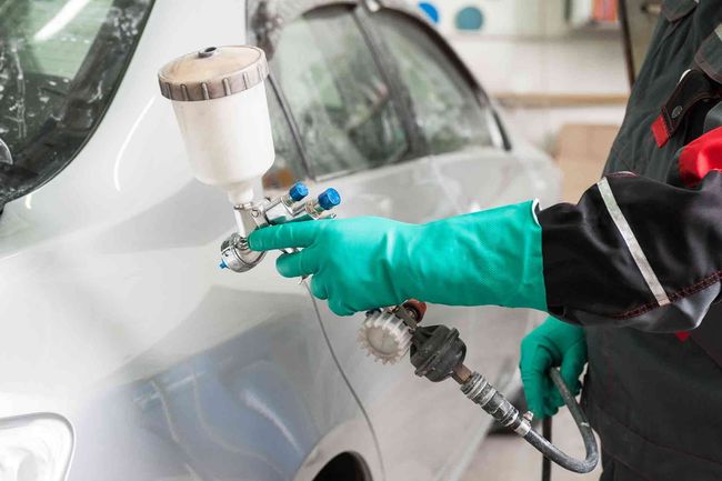 Person in green gloves spray painting a car white in a workshop.